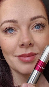 a woman is holding up a mascara tube