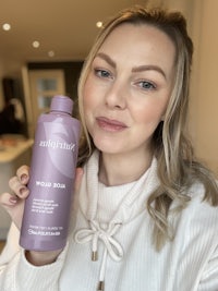 a woman is holding up a bottle of a product